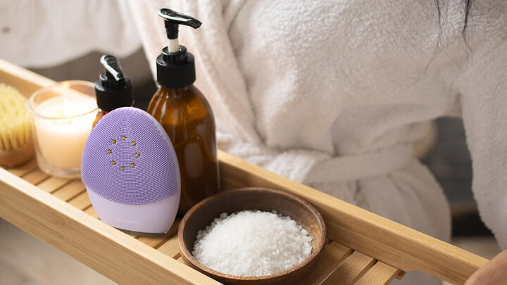 Swedish Beauty Routine with FOREO LUNA 4 Hands holding a wooden tray with bath salt, liquid soap, and FOREO LUNA 4