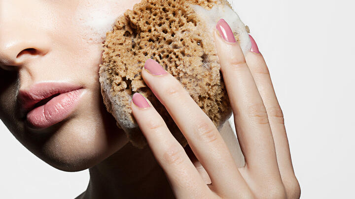 Face wash for clean pores A caucasian woman face closeup, holding a natural sponge with large pores and washing her face