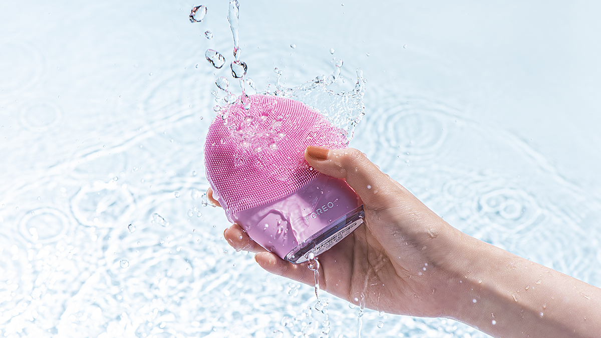 LUNA 4 plus is best for aging skin Hand holding FOREO LUNA 4 plus pink facial cleansing brush, surrounded by water