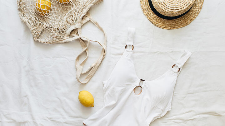 Travel selfcare White swimsuit, straw hat, and a natural bag with lemons on a white sheet