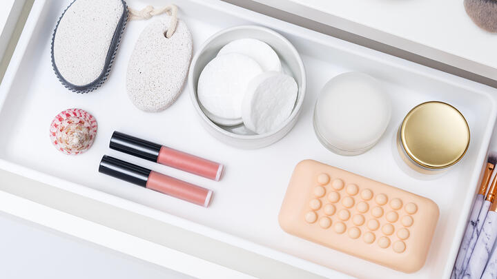 Decluttering tips for your skincare and makeup A cosmetic drawer with neatly organized soap, creams, cotton pads, pumice stone, pink lip gloss, and a sea shell